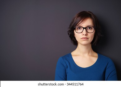 Serious Young Woman with Eyeglasses Looking Away Against Gray Wall with Copy Space on the Left Side.