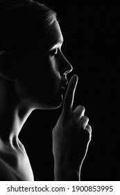 Serious Young Woman With Finger On Her Lips Show Silence Gesture On Black Background, Profile View, Monochrome