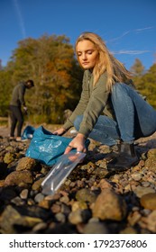 Serious Young Woman Picking Up Plastic At Rocky Beach