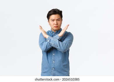 Serious-looking concerned asian male student showing forbid gesture, making cross sign to stop someone, disagree and prohibit action, telling no, enough, being fed up, standing white background - Shutterstock ID 2026510385