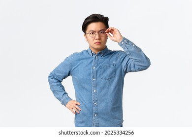 Serious-looking Suspicious Asian Male Entrepreneur Touching Glasses On Face And Frowning Doubtful, Standing Hesitant Or Skeptical, Dont Trust Someone, Posing Uncertain White Background