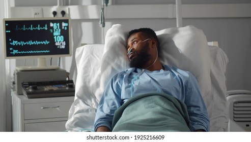 Seriously ill african man lying on bed in hospital with monitors showing his vital signs. Portrait of sad afro-amerian male patient resting in intensive care unit - Powered by Shutterstock