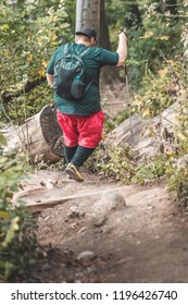 A Seriously Overweight Person Is Descending Down The Mountain Using Hiking Poles. Concept Photo Of A Man Loosing Weight While Hiking In The Mountains.