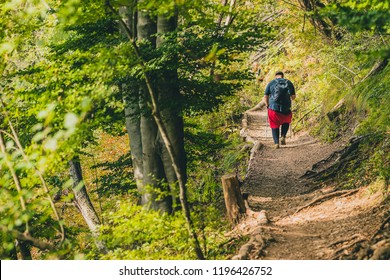 A Seriously Overweight Person Is Descending Down The Mountain Using Hiking Poles. Concept Photo Of A Man Loosing Weight While Hiking In The Mountains. Sport, Fitness And Health.