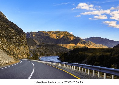 Serpentine asphalt road among high snow-capped mountain peaks, yellow desert, autumn green forest and blue sky. Car on the highway against the background of a mount landscape. - Powered by Shutterstock