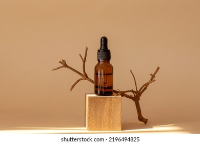 Serum in amber glass bottle with pipette on geometric wooden stand, 3d podium. Cosmetic moisturizing product in transparent package on brown background in rays of sunlight.