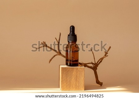 Serum in amber glass bottle with pipette on geometric wooden stand, 3d podium. Cosmetic moisturizing product in transparent package on brown background in rays of sunlight.