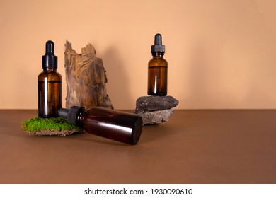 Serum Bottles On Brown With A Beige Background. Sustainable Lifestyle Concept, Natural Cosmetics. Cosmetic Product With Moss, Stones And Tree Bark Decor. Front View, Copy Space.