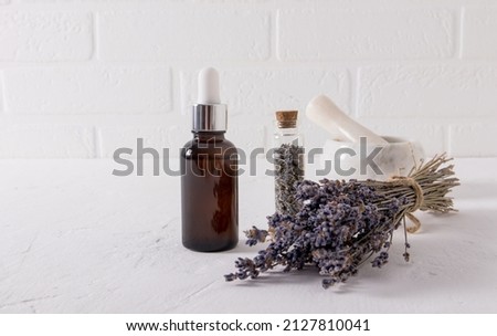 serum with an extract of lavender herbs for face and body skin care in a glassbottle on a white table and the brick wall