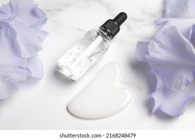 Serum With Floral Extracts For Skincare, Gua Sha Stone For Face Massage. Nature Cosmetics In Glass Bottle With Pipette And Iris Flowers. Face And Body Care Spa Concept.