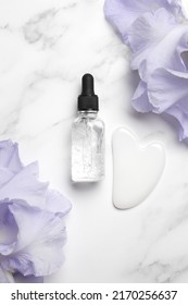 Serum With Floral Extracts For Skincare, Gua Sha Stone For Face Massage. Nature Cosmetics In Glass Bottle With Pipette And Iris Flowers. Face And Body Care Spa Concept.