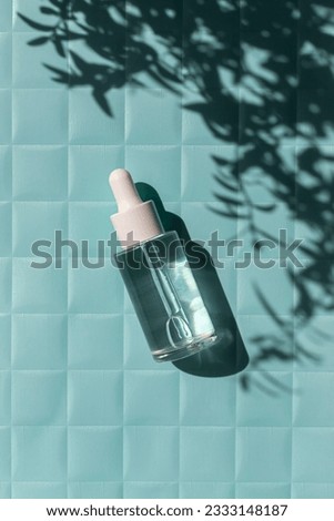 Serum glass bottle on the water texture on blue paper checkered texture background on the noon sunlight with leaves shadow. 