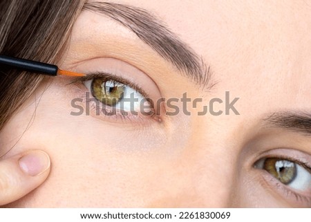 Serum for growth and density of eyelashes with oils and peptides. Close-up of a girl's eyes with a serum brush. The eyes of a young woman in close-up. The concept of preventing hair loss.