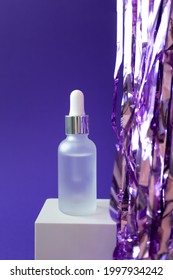 Serum Mockup With Pipette And Holiday Tinsel On Cube Podium On Violet Background, Vertical. Treatment Spa Beauty Skin Care Cosmetic Product