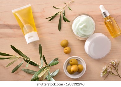 Serum and moisturizing cosmetic cream with olive extract for skin with branch and olives on wood table. Top view.