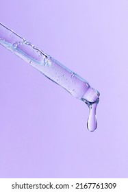 Serum Pipette Close-up With Falling Drop On Purple Background 