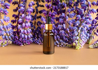 Serum in unbranded brown glass bottle with pipette and blue purple lupine flowers on brown golden background. Cosmetic bottle blank with hyaluronic acid for branding. Mockup, template, care skin.