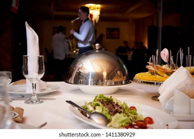 Mesa de cena.Plato caliente en la cúpula de la mesa del servidor sobre un fondo borroso que toca saxofonista a los huéspedes.