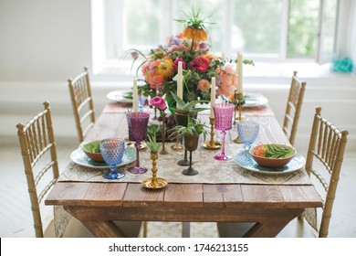 Served table for festive dinner in style boho chic. Decor from fresh flowers peonies, roses, orchids and Leucospermum conocarpodendron surrounded by dishes of plates, glasses and candles. Top view.