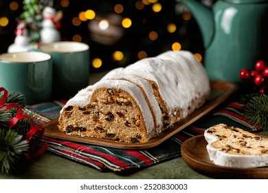 Served table with Stollen cake, tea cups and pot. German Christmas dessert, bread chock full of dried fruit, candied peel, and almonds. Festive lights, tree and decoration. - Powered by Shutterstock