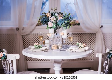 Served table for two with bouquet of spring flowers. Interior design of white room with beautiful decor. Big windows at the background. Frontal.