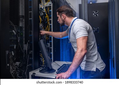 Server checking. Young bearded man in tshirt and jeans with badge in server room near open cabinet checking