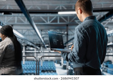 Server farm engineer using laptop to visualize AI model outputs on screen. IT professional using notebook to upgrade enterprise data center rigs generating AI visualizations