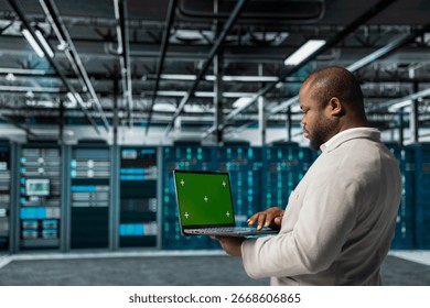 Server farm system administrator using mockup laptop to repair equipment storing datasets. African american man using green screen notebook to do debugging on rigs doing computational operations