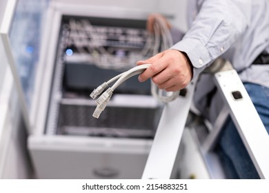 Server Hardware Setup. Male Worker Configures Local Network By Holding Cables And Plugs To Connect To Server. Close Up Of Plug In Hand Of Man Standing On Ladder.