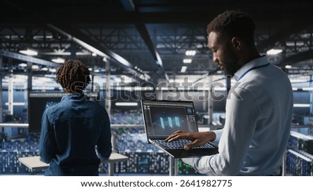 Server hub coworkers visualizing large language model architecture using notebook. Data center technicians on industrial platform collaborating on neural network software tasks using laptop