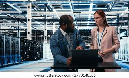 Server hub engineering team using laptop to monitor power consumption, cooperating, data center coworkers brainstorming, overseeing hardware, ensuring industry standards compliance, camera A.