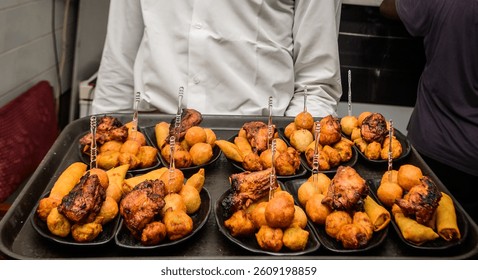 Server presenting assorted Nigerian small chops platter, featuring puff-puff, grilled chicken, samosas, and spring rolls at a social event in Lagos