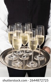 Server presenting multiple glasses of champagne on a silver tray, ready for guests at a celebration or reception.