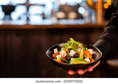 Server presenting a vibrant, fresh salad in a black bowl against a blurred restaurant background - Powered by Shutterstock