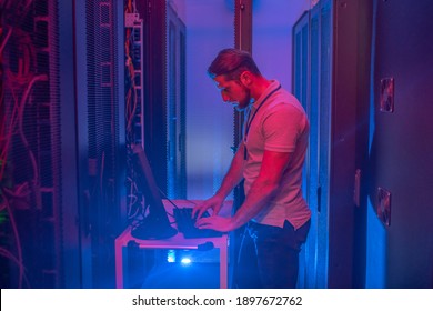 Server Room. Man In Tshirt And Jeans Working On Computer In Dark Server Room With Blue Backlight