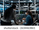 Server room manager overseeing work done by engineer using artificial intelligence to reduce downtime. Team leader supervising employee implementing AI driven solutions for data center equipment