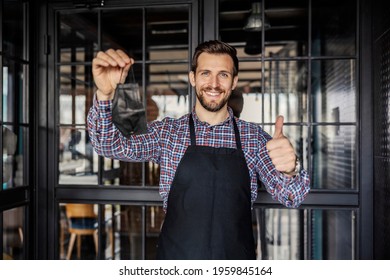 A Server Wears A Face Mask During A Corona Virus. A Waiter In Uniform And With A Protective Face Mask Stands In Front Of The Entrance To The Restaurant And Correctly Places And Points To The Mask