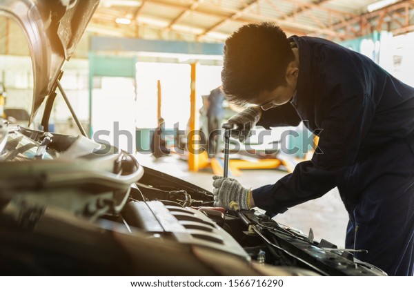 Service\
Car Bonnet Mechanic. Asian man auto mechanic using a wrench and\
screwdriver to working service car in the\
garage.