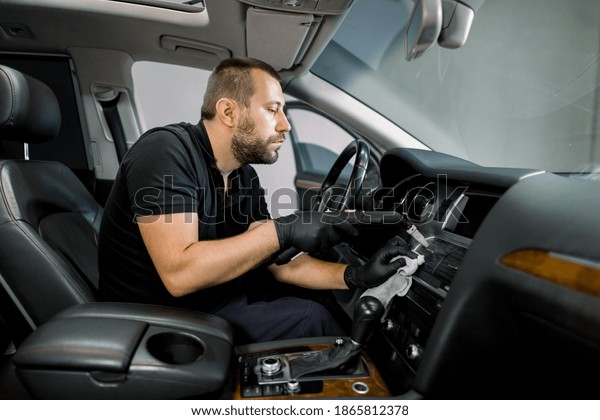 Service cleaning of air conditioner of the car\
with hot steam. Concentrated professional Caucasian male worker in\
black uniform, sitting in front seat of modern car and using hot\
steam cleaner