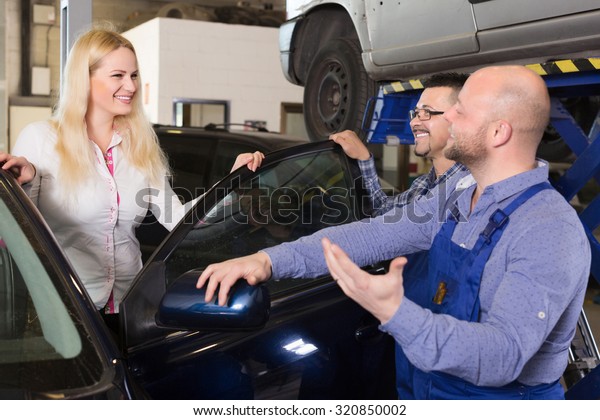 Service crew and driver standing near car and\
smiling. Focus on woman
