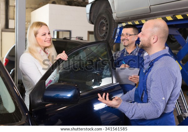 Service crew and satisfied woman driver\
standing near car and smiling. Focus on\
woman