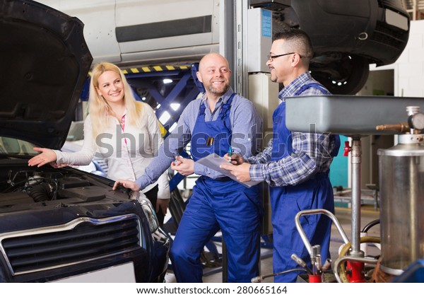 Service crew and woman driver standing near car and\
smiling. Focus on man