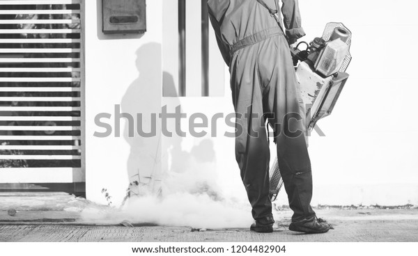 Service Employee pest control man in uniform\
trying killing insects and fogging to eliminate mosquito for\
preventing spread dengue fever and zika virus.Worker fogging\
residential area with\
chemical.