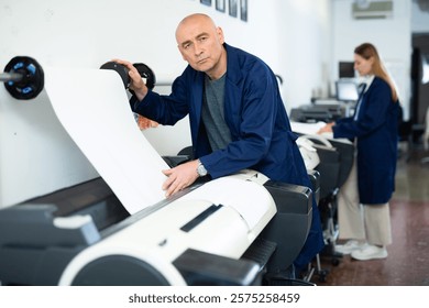Service man uses plotter and checks the functionality in printing shop