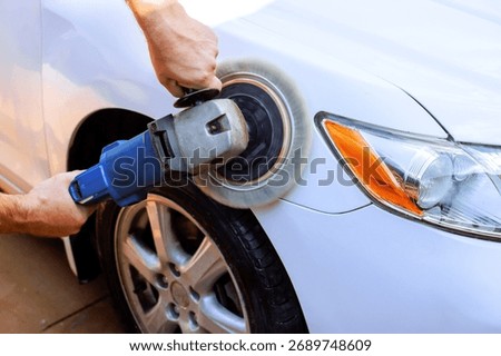 Service man using buffer to polish surface of white car in enhancing its shine appearance.