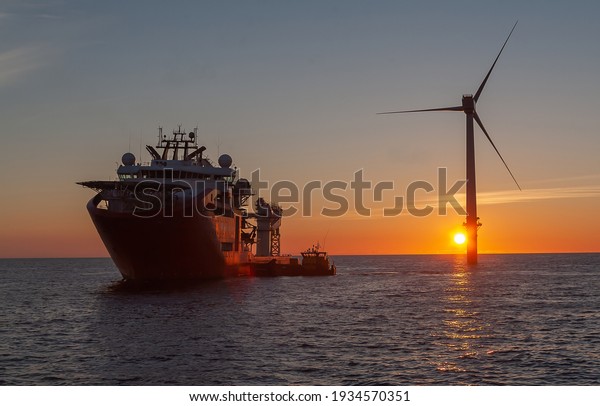 Service operational vessel, with\
crew transfer vessel alongside and sun setting on wind\
turbine