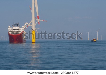 Service operational vessel in dynamic position mode alongside wind turbine with small crew transfer vessel operating in the field