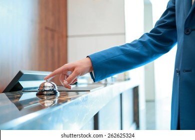 Service, please. Closeup of a businessman hand ringing silver service bell on hotel reception desk - Shutterstock ID 262625324