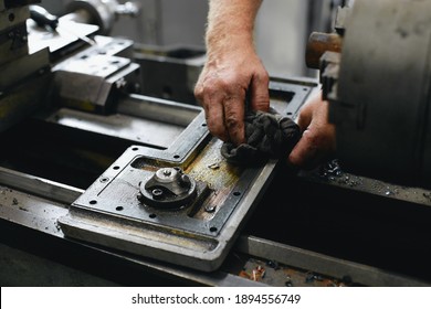 Service and repair of machine tools in a machine shop or workshop. These are the hands of a white man with a rag wiping the metal parts of a lathe engine with grease. The work of a locksmith on