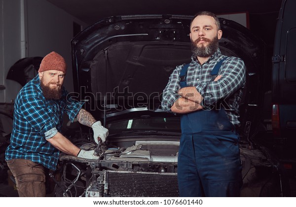 Service station. Two bearded brutal mechanics\
repairing a car in the\
garage.
